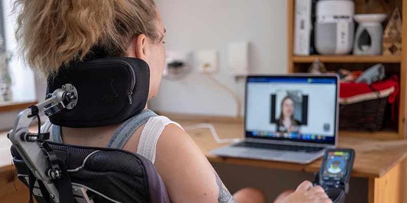 Woman in electric wheelchair using built in accessibility features to understand a streamed public meeting.