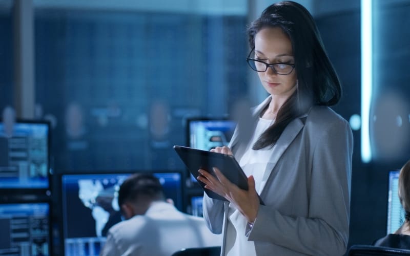 A woman looks at her iPad while people work on computers in the background.