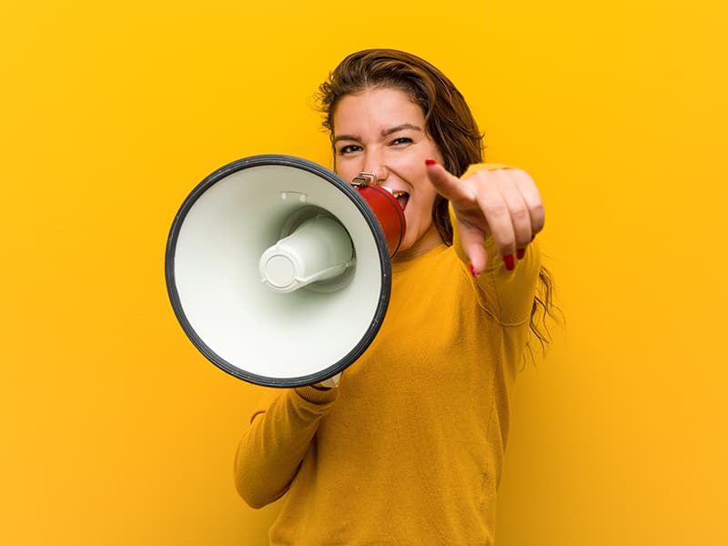 Young woman smiling and speaking into a megaphone while pointing forward, symbolizing game-changing updates to government technology.