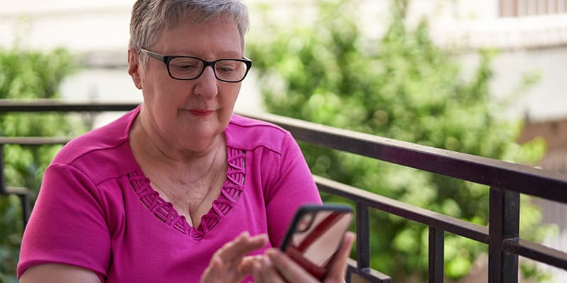 Older Caucasian woman in her 60s using a smartphone on her home balcony to access digital government services.