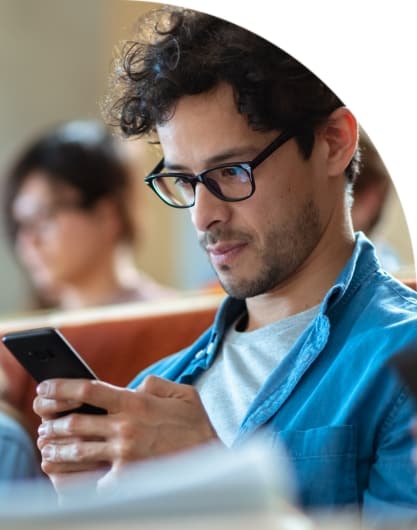A student staring down at his mobile phone, receiving a digital communication, while in a lecture hall.