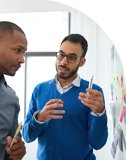 A man holding a marker next to a white board, planning strategic experience services with a colleague.