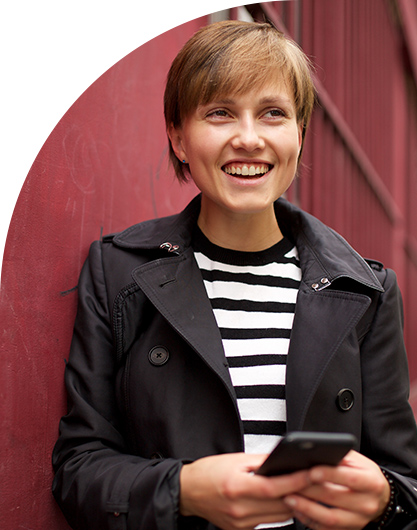 Woman wearing a striped shirt and holding a phone while leaning against a red barn.