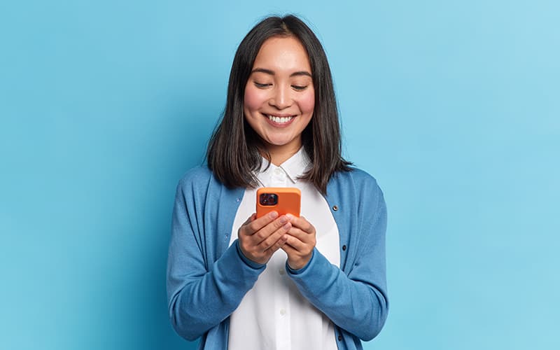 Asian American woman wearing blue communicating with her local government through Government Experience Agent (GXA) on her orange mobile phone