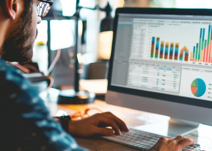 A person at desk viewing colorful data charts on a computer screen in an office setting.