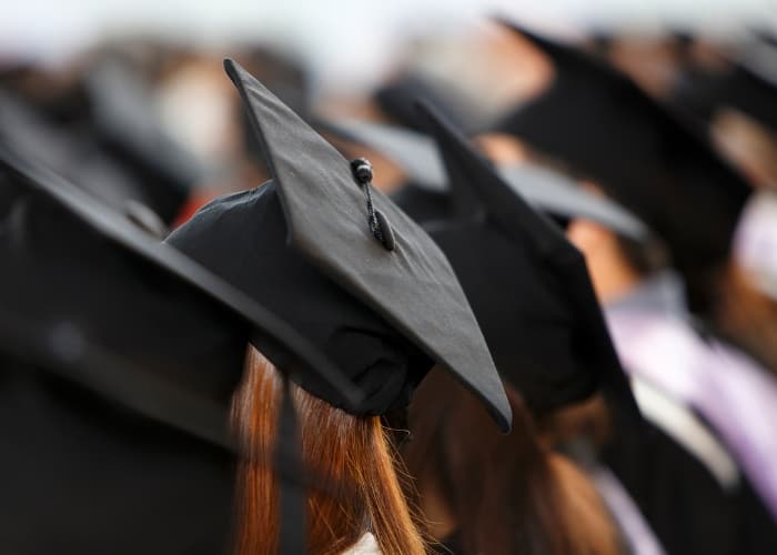 Group of graduates wearing black mortarboard caps with tassels, viewed from behind at a commencement ceremony.