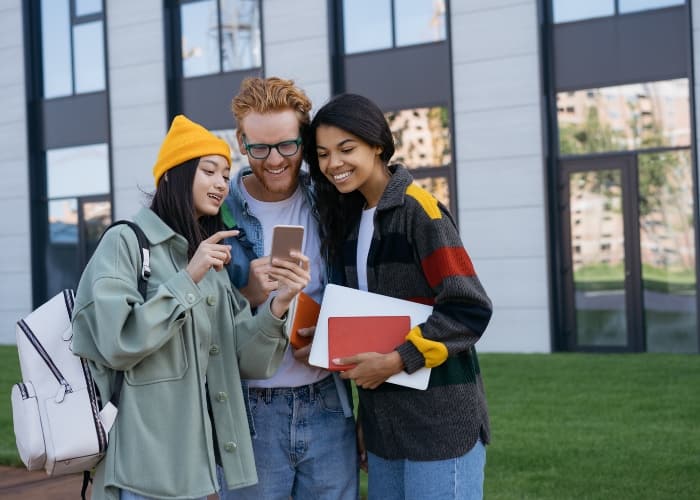 University students outside a campus building, looking at a smartphone together.