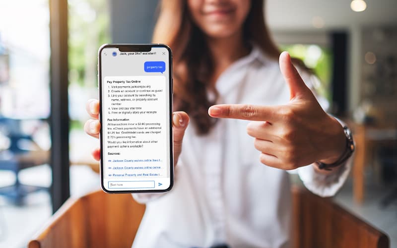 A person holds a smartphone displaying a webpage about paying property tax online, with their other hand pointing at the screen.