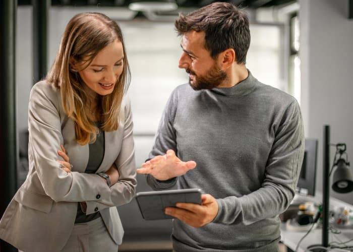 Two people in a professional setting, with one holding a tablet and explaining something to the other.