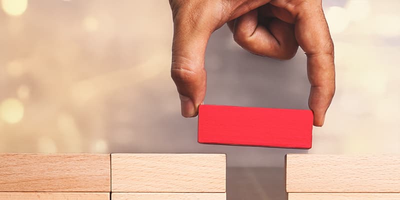 A man placing a bright red block to bridge the gap between two stacks of wooden blocks.