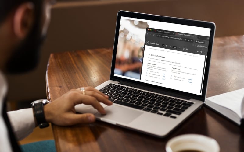 A person browses through a benchmark report on their laptop while simultaneously watching a webinar.