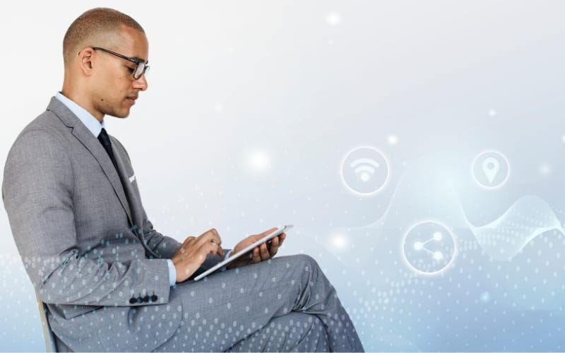 A man sitting in a chair, scrolling through a tablet with graphic icons floating to the right.