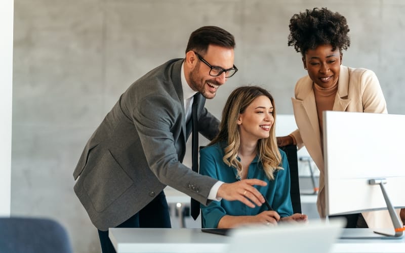 Three people smiling as they look at a computer monitor.