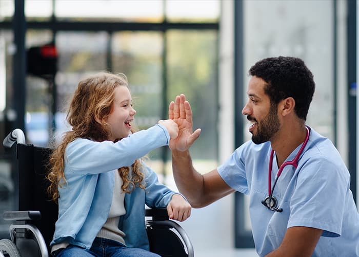 Child in wheelchair giving a doctor a high-five.