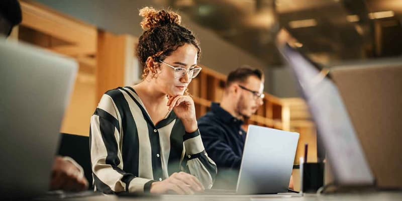 Two people working on laptops in a softly lit office.