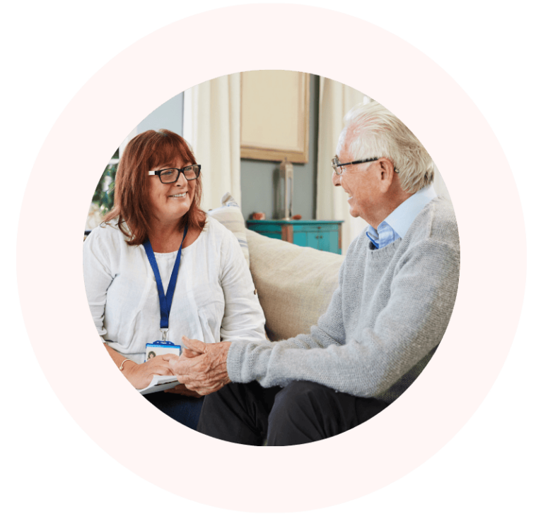 A woman wearing a name badge talks with an eldery man on a couch.